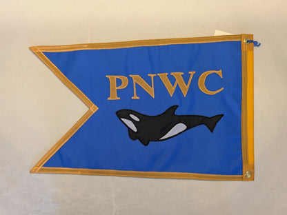 A blue pennant flag with gold trim, featuring the gold letters 'PNWC' and a black-and-white orca illustration, displayed against a light beige background.